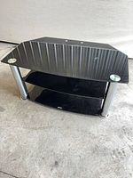 Front angled view of smoked glass TV stand showing three-shelf configuration and chrome legs