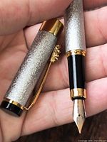 Pen uncapped showing nib, textured silver body, gold clip, black finial