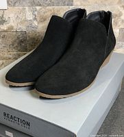 Front angled view of both black suede ankle boots on box