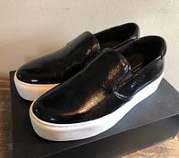 Angle view of both black patent slip-on loafers on box