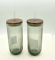 Two ribbed glass tumblers with wood lids and straws front view