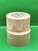 Two stacked rolls of tan flatback tape in shrink wrap
