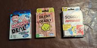Front view of three boxed card games: Monopoly Deal, Silent But Deadly, Sorry! Revenge