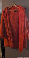 Full view of orange Alpinetex winter coat hanging, showing hood, length and interior lining