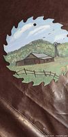 Full view of painted circular saw blade showing barn scene