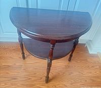 Front angled view of demilune side table showing turned legs and lower shelf