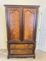 Front view of closed armoire showing doors, lower drawers, veneer, hardware, carved feet