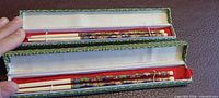 Open boxes showing two pairs of cloisonné chopsticks with red felt lining