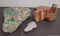 Three specimens: green mineral, reddish fossil matrix, grey fossil piece