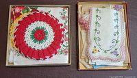 Two shallow boxes showing folded linens topped by crocheted doily and embroidered linen piece