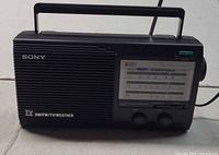 Front view of Sony ICF-34 radio showing grille, tuning window, knobs, handle and antenna