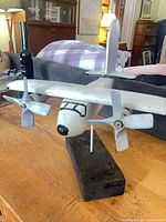 Front three-quarter view of wooden plane on stand, shows propellers and fuselage details