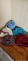 Five handmade knit/crochet items laid out: four beanies and a rolled scarf