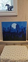 Front view of blue city skyline painting with moon