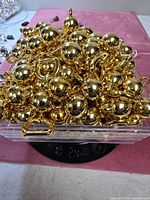 Plastic bin of gold-tone ball connectors and D-rings on scale reading 9.34 lb