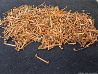 Large pile of copper-tone brooch pin backs on black surface