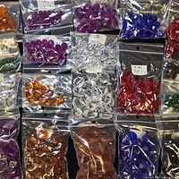 Multiple bags of assorted coloured faceted beads laid out in grid