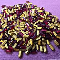 Pile of ruby red rectangular rhinestones with gold foil backs on pink surface