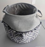 Fabric storage basket showing geometric exterior, cuff, handles, and pom-pom trim