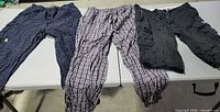 Overview of three men’s bottoms laid out: two plaid lounge pants and one black cargo shorts