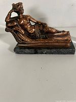 Side view of copper-tone reclining female figure sculpture on dark stone base
