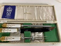 Open box showing three utensils with porcelain handles and gold decoration