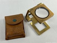 Brass folding magnifier and leather case side by side