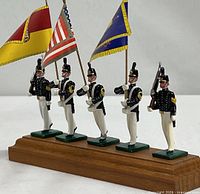 Front view of five toy soldiers on wood stand with three flags
