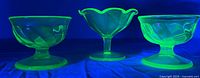 Three uranium glass dessert dishes glowing under UV