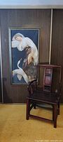 Framed painting displayed on wall beside chair for scale