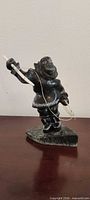 Full view of stone Inuit hunter sculpture with bone harpoon and string on wooden surface