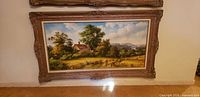 Full view of framed pastoral landscape print leaning against wall
