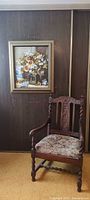 Framed floral painting displayed above chair for scale