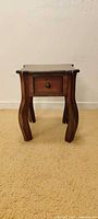 Front view of wooden side table showing drawer and curved legs