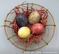 Top view of four marble eggs arranged in gold-tone wire basket with red filler