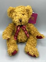 Front view of jointed caramel plush bear with ribbon and tag