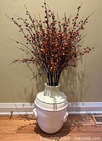 Vase with inserted faux berry branches against wall