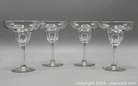 Front view of four identical clear glass margarita glasses on a plain background