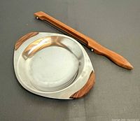 Stainless steel dish with teak accents and bread knife handle visible