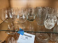 Group of stemless wine glasses, rocks tumbler, highball tumblers, ribbed bud vase on glass shelf