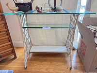 Full view of console table showing glass top, middle glass shelf, wood bottom shelf, white cast iron base