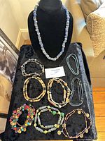 Group shot of all necklaces and bracelets laid on black cloth with bust display