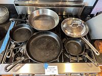 Group of five cast iron skillets, stainless sauté pan and lid on stovetop