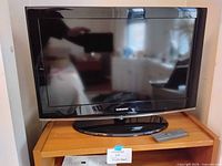 Front view of Samsung TV on wooden stand with remote visible