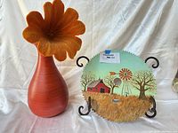 Vase with felt flower beside painted saw blade on stand