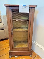 Front view of cabinet showing chicken-wire door, shelves, brass feet