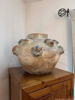 Front view of stoneware vase on cabinet showing applied animal heads and textured surface