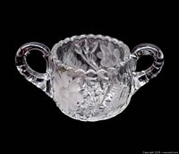 Front view of clear cut glass double-handled sugar bowl showing daisy motifs and scalloped rim
