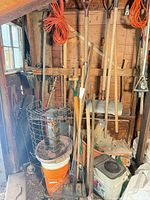 Overall view of assorted long-handled tools, cords, bucket, cage in garage corner