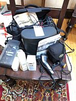 Overview showing camcorder bag with JVC manual, Fujifilm camera, RadioShack adapters, charger, clipper, flashlight